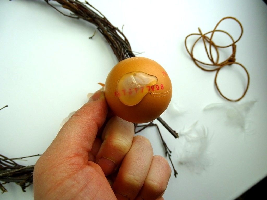 Klebe die Eierschalen mit Heißklebepistole auf den Osterkranz aus Birkenzweigen.