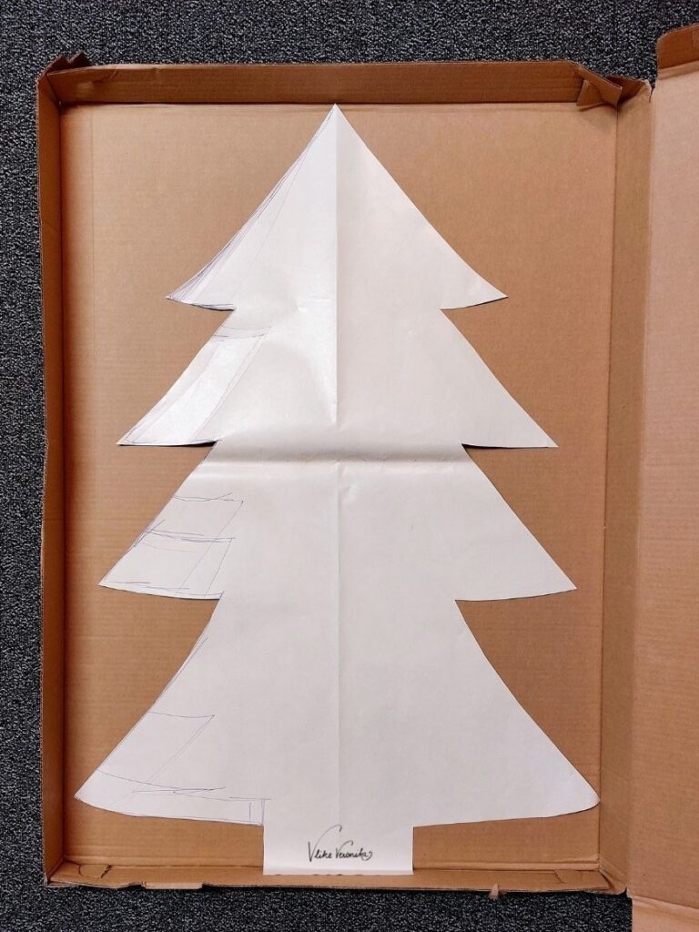 Lege den Weihnachtsbaum aus Papier auf die Wellpappe auf.