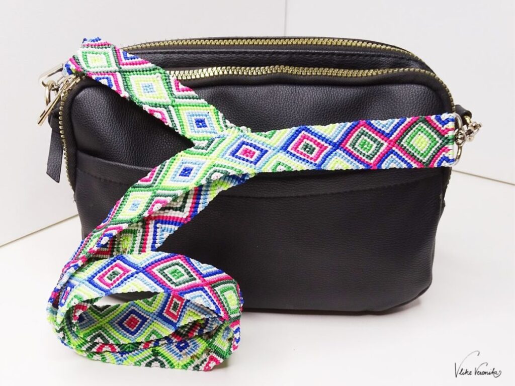 Der bunte, breite Taschengurt aus Nylonfaden ist robust und ein schöner Kontrast zur schwarzen, kleinen Handtasche.