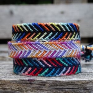 Drei Armbänder mit geknüpftem Farnmuster liegen auf einer hölzernen Palettencouch im Garten.