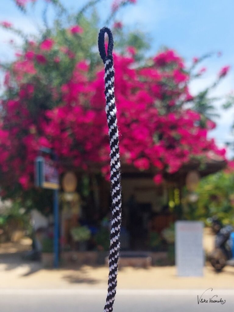 Ein schwarz-weißes Kumihimo-Style Armband vor dem rosa Blütenstrauch eines Hotels ins Sri Lanka.
