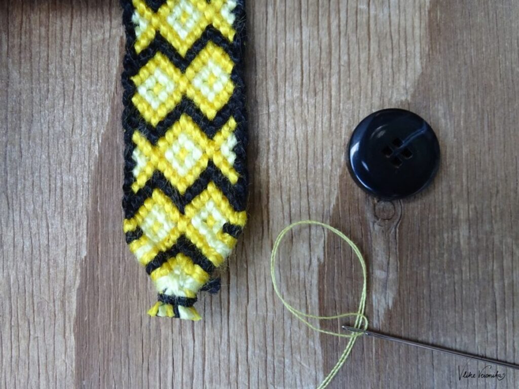 Der Knopfverschluss kann auf einem geknüpften Bandende angenäht werden.