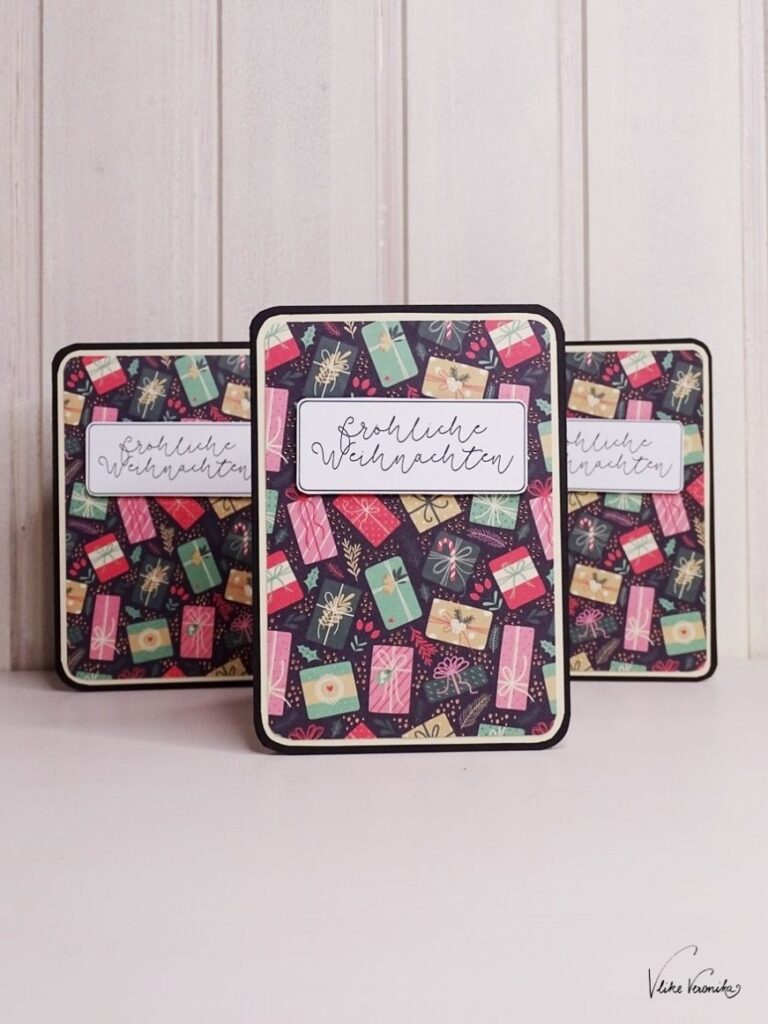 Schwarze Weihnachtskarte mit bunten Geschenken und Fröhliche-Weihnachten-Schriftzug.